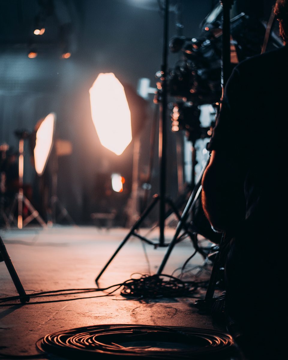 A film set between takes: light stands, coiled cables and a crew member in silhouette.